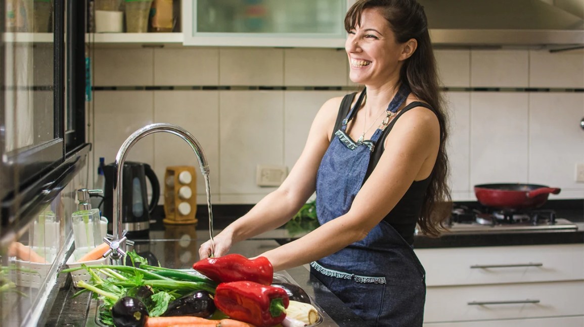 A person smiles while preparing a meal in their kitchen.